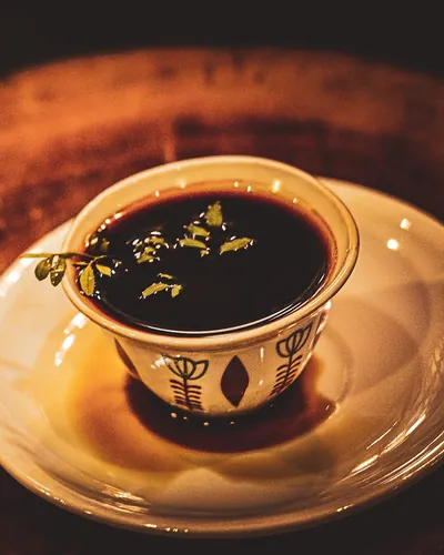 A cini cup of black coffee with rue leaves on a saucer