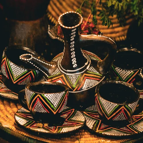 Hand-painted cini cups with zigzag patterns around a small jebena on a woven tray