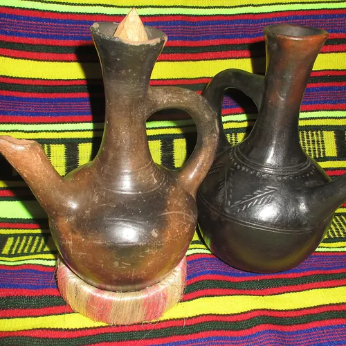 Two clay jebena coffee pots, one brown and one black, on a striped woven cloth