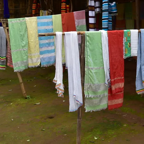 Handwoven Dorze cotton scarves in mint, sky blue, coral and white drying on a wooden rail