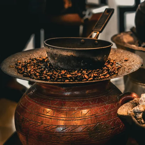 Coffee beans roasting in a pan on top of an engraved copper pot