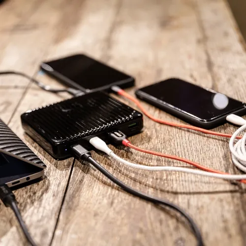 A black power bank charging two phones and a laptop on a wooden table