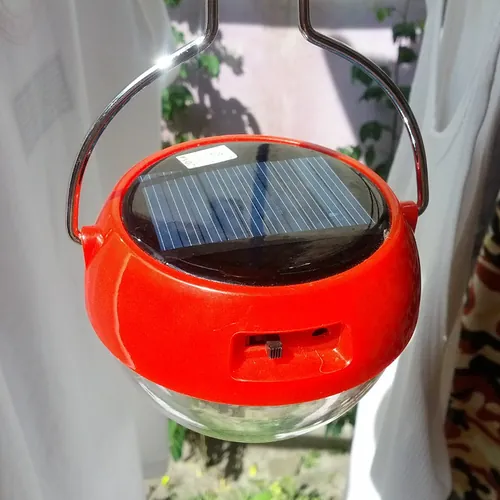 A red solar lantern with a solar panel in its lid, hanging from a wire handle